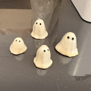 Four large ceramic figurines shaped like ghosts with black eyes from the &ldquo;Lily Strider - Old Town ghosts - Large&rdquo; collection are arranged on a dark, reflective surface. Reminiscent of the mysterious Old Town ghosts often mentioned by Lily Strider, these figures exude an air of intrigue and charm. Gate21.ee