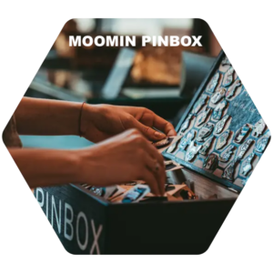 A person’s hands pick a pin from a box filled with assorted pins. The box, labelled "Moomin - PINSBOX - KÕIK," has white lettering displayed at the top of the image. Gate21.ee