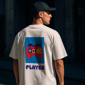 Wearing the Player - PROJECTION Ts in white, which features a vibrant game controller graphic and &ldquo;PLAYER&rdquo; printed on the back, an individual stands outdoors in a shaded urban area with their back to the camera, also wearing a black cap. Gate21.ee