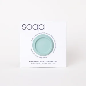 A circular Soapi - Mint magnetic soap holder in light green is centred in white packaging labelled “soapi.” The minimal, modern design features clean lines, with product highlights about recycled materials and features printed in both English and German. Gate21.ee