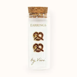 A pair of small, brown Brezel earrings by Vivi is displayed on a card inside a clear glass jar with a cork stopper, set against a plain, light-coloured background. Gate21.ee