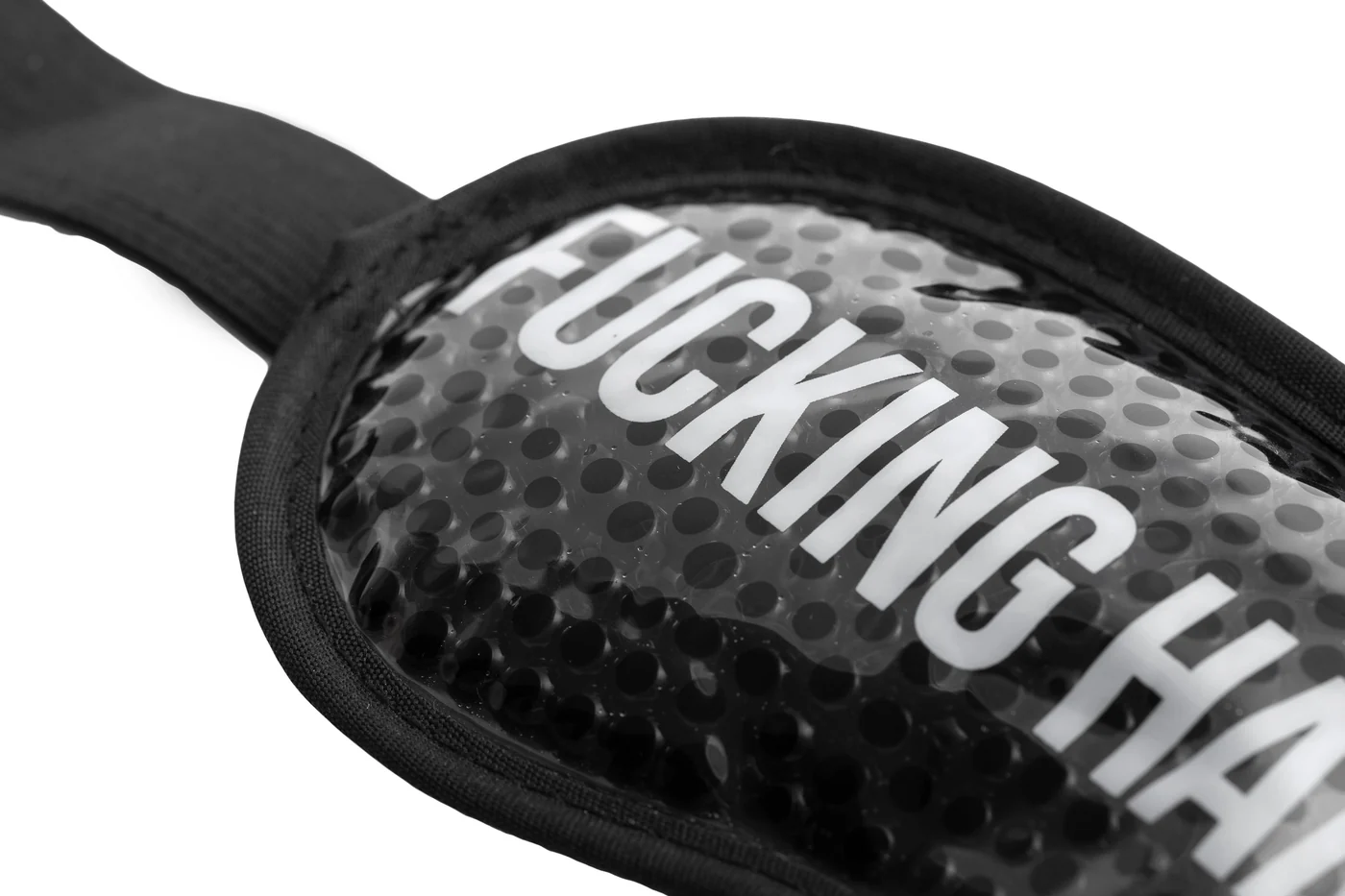 A close-up photo of the “Fucking Hangover” gel eye mask, a bold black padded mask with a textured surface and strap, featuring partially visible white text reading “FUCKING HA...”. Gate21.ee