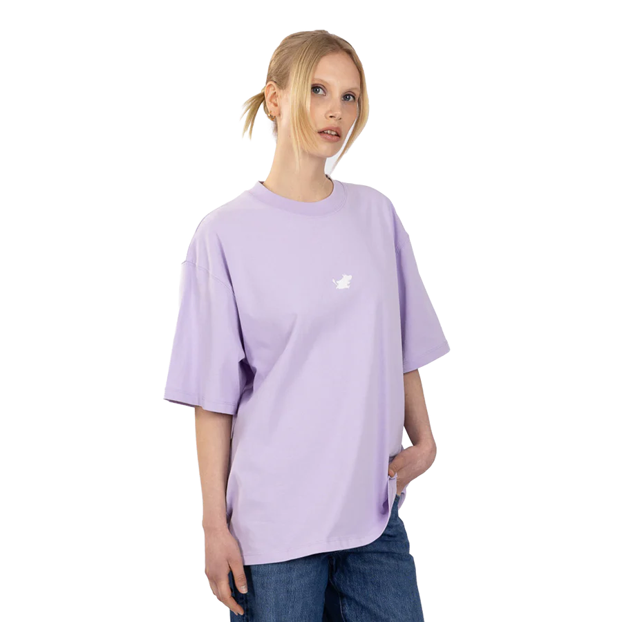 A person with fair hair styled in a low ponytail wears the loose-fitting Lavender Moomin Heavy T-shirt, which features a small white graphic on the chest, paired with blue jeans against a plain white background. Gate21.ee