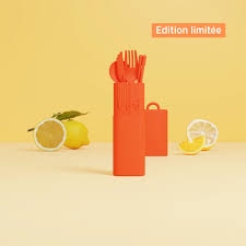 A Bini Cutlery Kit - Sunset (Limited Edition) in a striking orange hue stands upright on a yellow surface with lemons in the background, reflecting the warm tones of sunset. In the top right corner, a label reading “Édition limitée” emphasises its exclusive Limited Edition status. Gate21.ee