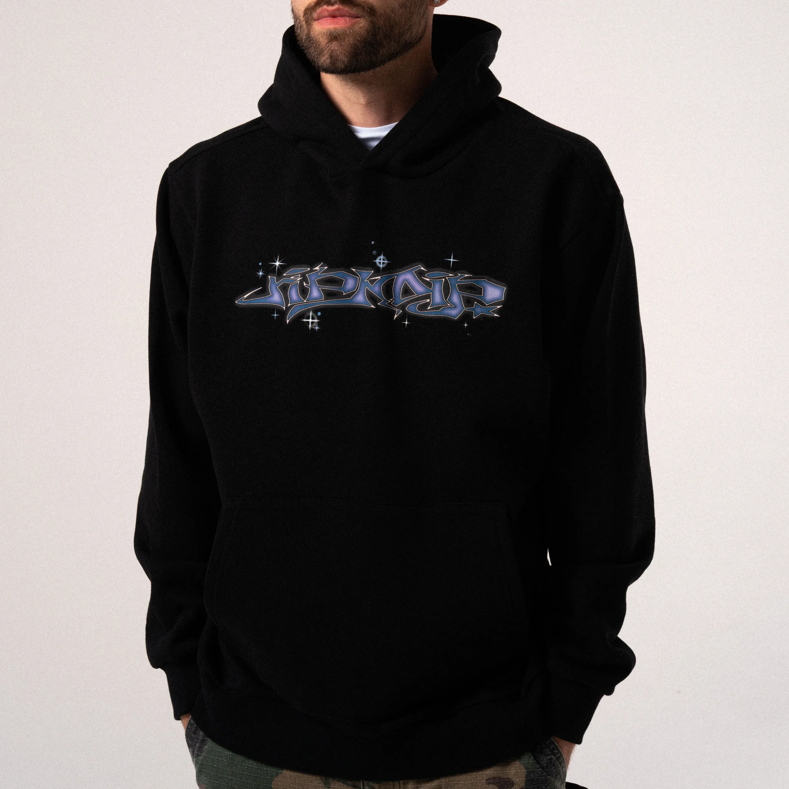 A person wearing the Big Poe Hoodie - Black by Ripndip, featuring stylised blue graffiti-style text and small star-like accents on the chest. The person has a trimmed beard and is standing against a plain, light background. Gate21.ee