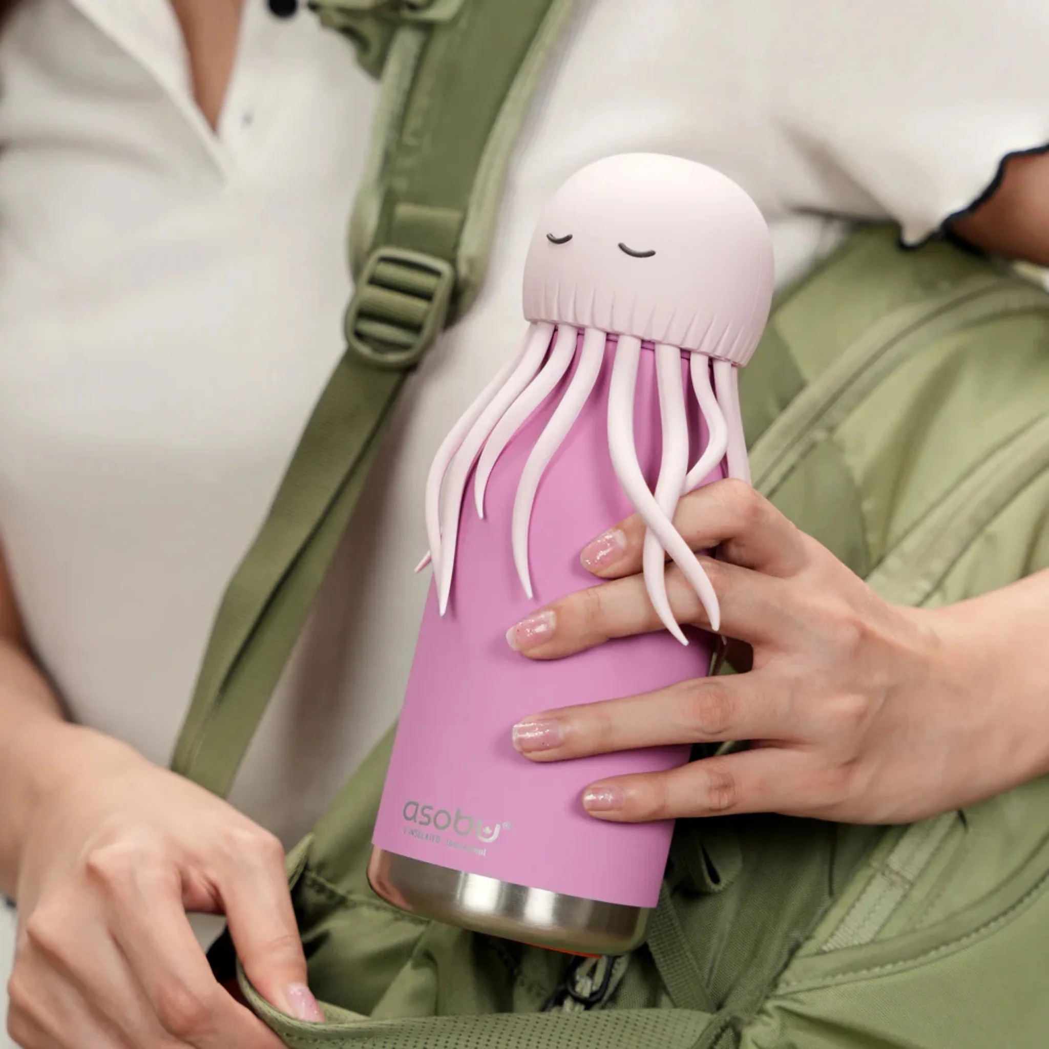 A person holds the Octopus Bestie - 740ml, a pink ASOBU water bottle with a lid shaped like a cartoon octopus complete with tentacles and a face, as they place it in a green rucksack. Gate21.ee