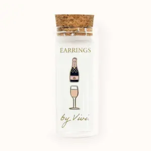 A clear glass vial with a cork lid contains two “Champagne earrings by Vivi”: one earring shaped like a champagne bottle and the other like a wine glass. Gate21.ee