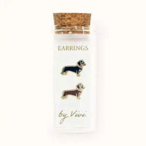 A clear glass vial with a cork lid contains two dachshund-shaped earrings—one black and one brown—labelled “Champagne earrings by Vivi” on the front in gold text. These charming earrings add a touch of whimsy to any accessory collection. Gate21.ee