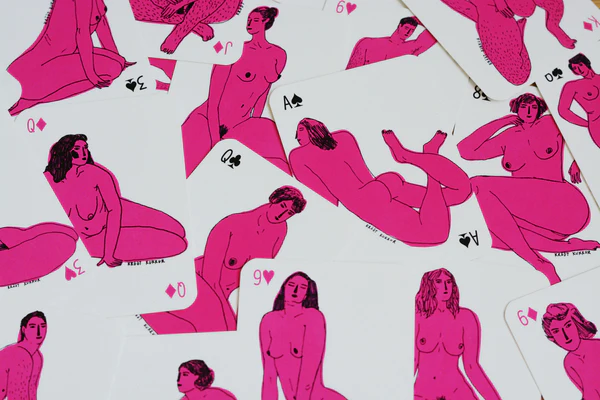 A scattered pile of Krõõt Kukkur Playing Cards - Nudes features illustrations of nude women in various poses, drawn in bold pink and black outlines. Designed by Krõõt Kukkur, these cards display nudes across different suits and values. Gate21.ee