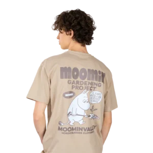 A person with short curly hair wears the charming “Moomintroll Ts – Gardening”—a beige Moomin T-shirt featuring a Moomin character with a spade and plant. The shirt reads: MOOMIN GARDENING PROJECT MOOMINVALLEY NORDICBUDDIES CLOTHING. Gate21.ee