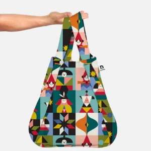 A hand holds a Notabag Playground – Special Edition reusable tote bag, featuring a colourful geometric and abstract pattern with various shapes and stylised human figures on a white background. Gate21.ee