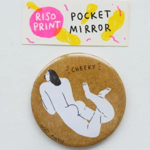 A round pocket mirror, inspired by Krõõt Kukkur Playing Cards – Nudes, features an illustration of a reclining nude figure in Krõõt Kukkur’s playful style with CHEEKY written above. The packaging reads RISO PRINT POCKET MIRROR and is decorated with yellow shapes on a white background, evoking the bold graphics typical of vintage playing cards. Gate21.ee