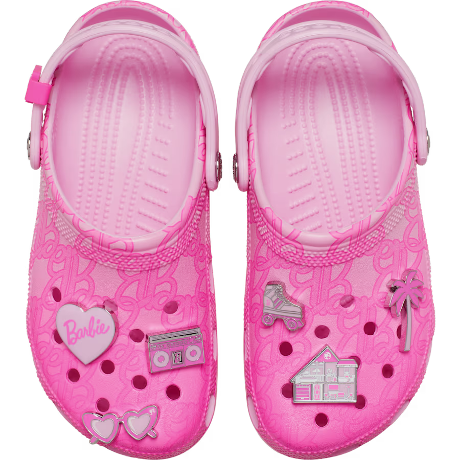 The Crocs Barbie® Classic Clog features a light pink design with embossed Barbie logos and comes adorned with six Barbie-themed charms—including a heart, boombox, house, car, and glasses—attached to the shoe holes. Gate21.ee