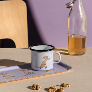 A 2.5dl Sniff – Moomin enamel mug featuring a charming rabbit design rests on a matching tray atop a light table. Walnut pieces lie nearby, alongside a glass bottle filled with amber liquid and a wooden chair in the background, all softly bathed in sunlight. Gate21.ee
