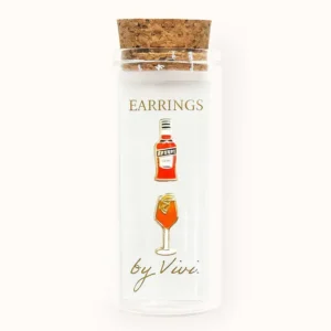 A clear glass jar with a cork lid, labelled “F*ck You earrings by Vivi” in gold text, holds two enamel earrings—one shaped like a red liquor bottle and the other like a cocktail glass. Gate21.ee