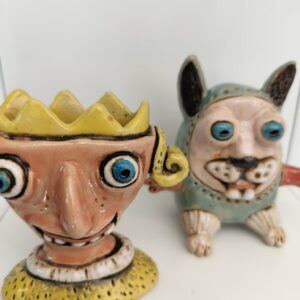 Two vibrant Raivo Koit kujud ceramic figurines displayed on a white surface: one features a yellow crown and wide eyes, whilst the other resembles an animal with blue fur, large eyes, and upright ears. Both showcase the artist&rsquo;s signature exaggerated, whimsical style. Gate21.ee