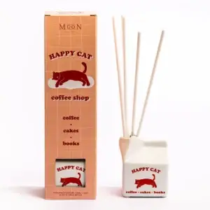 The “Happy Cat - 100ml Diffuser” from Wick & Vessel is a coffee shop-inspired home fragrance set, featuring a carton-shaped container with four reeds. Both the box and container are decorated with a red cat graphic and text that highlights coffee, cakes, and books. Gate21.ee